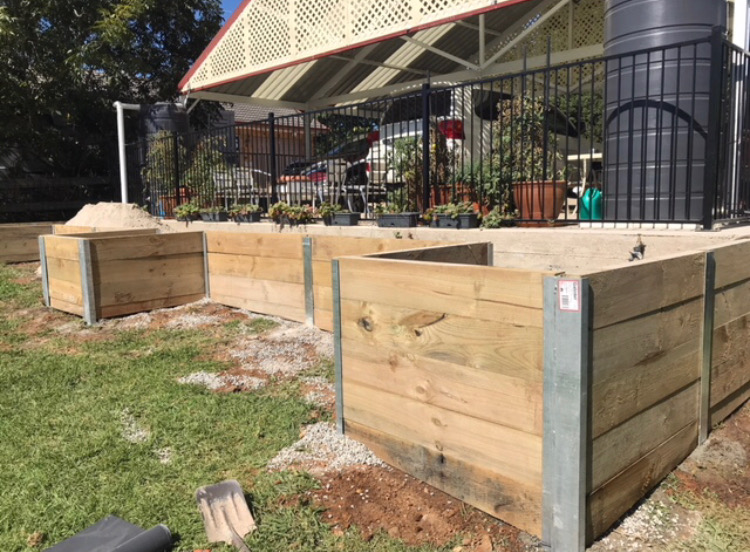 Two large timber sleeper raised planter boxes built as garden beds beside an outbuilding.